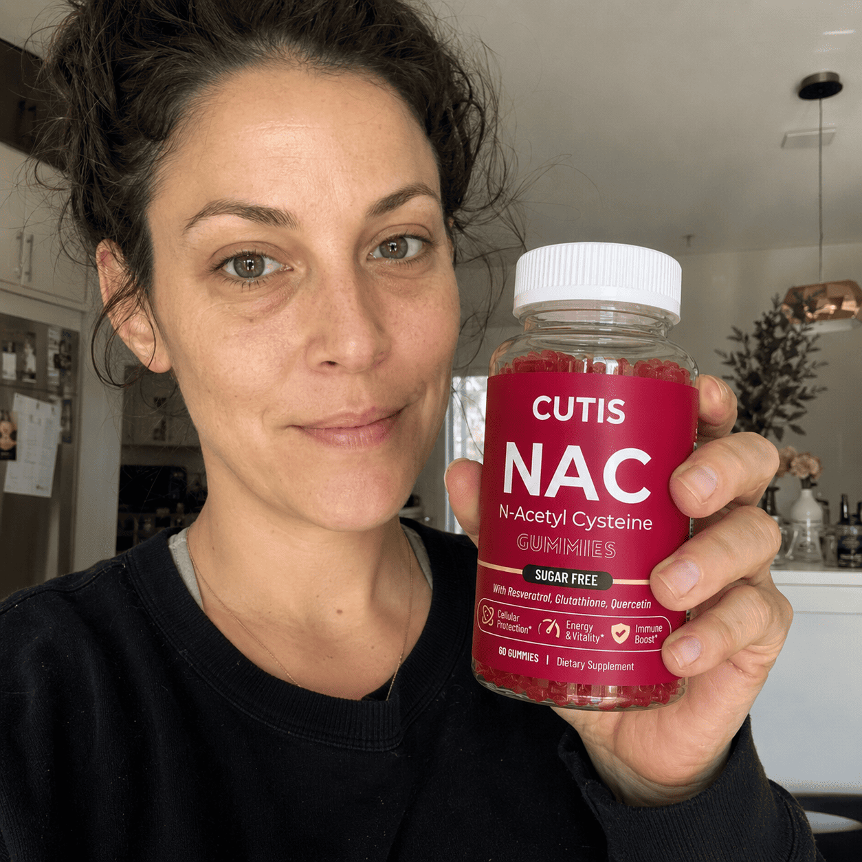 Woman holding a bottle of Cutis NAC supplements in a kitchen setting